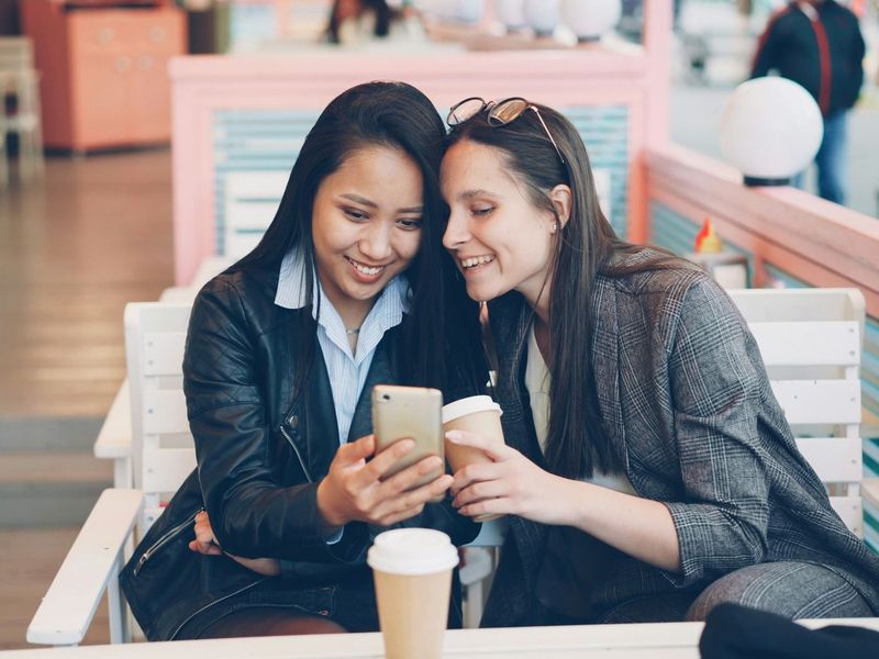 Dos amigas sonríen mientras miran juntas un celular en un café